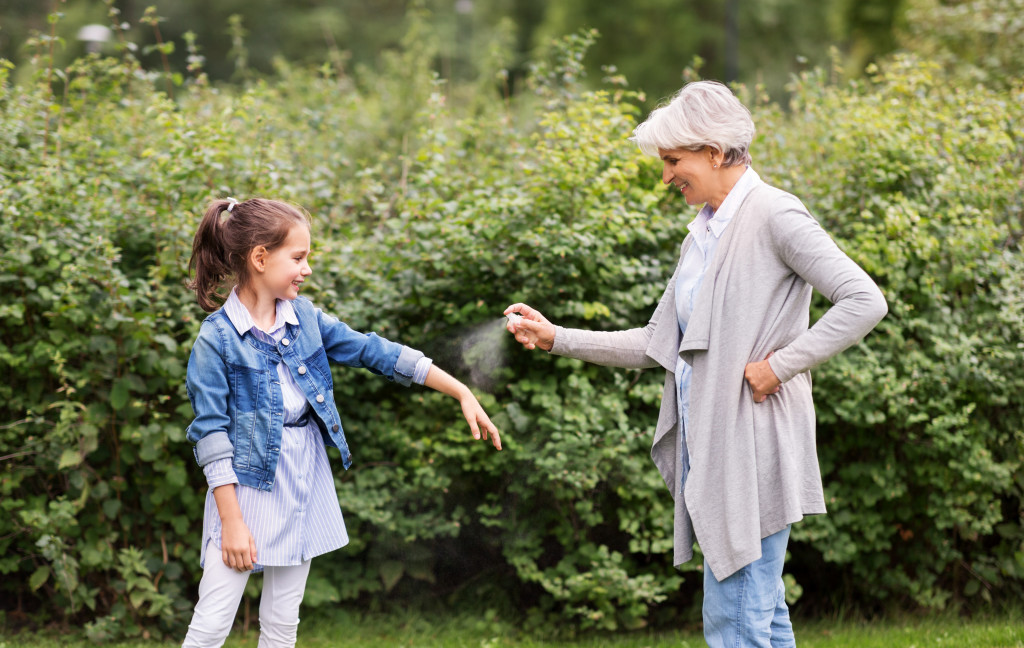 A mature woman spraying a repellent to a little girl