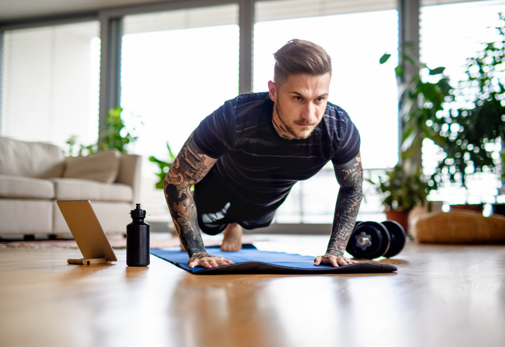 man with tattoos doing workout at home while watching from tablet